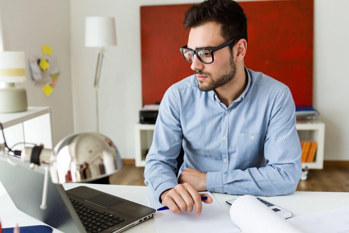 apuesto-joven-empresario-trabajando-ordenador-portatil-oficina